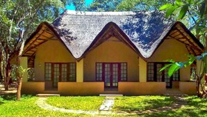 Una casa tradicional con techo de paja, rodeada de un césped cuidado y árboles.