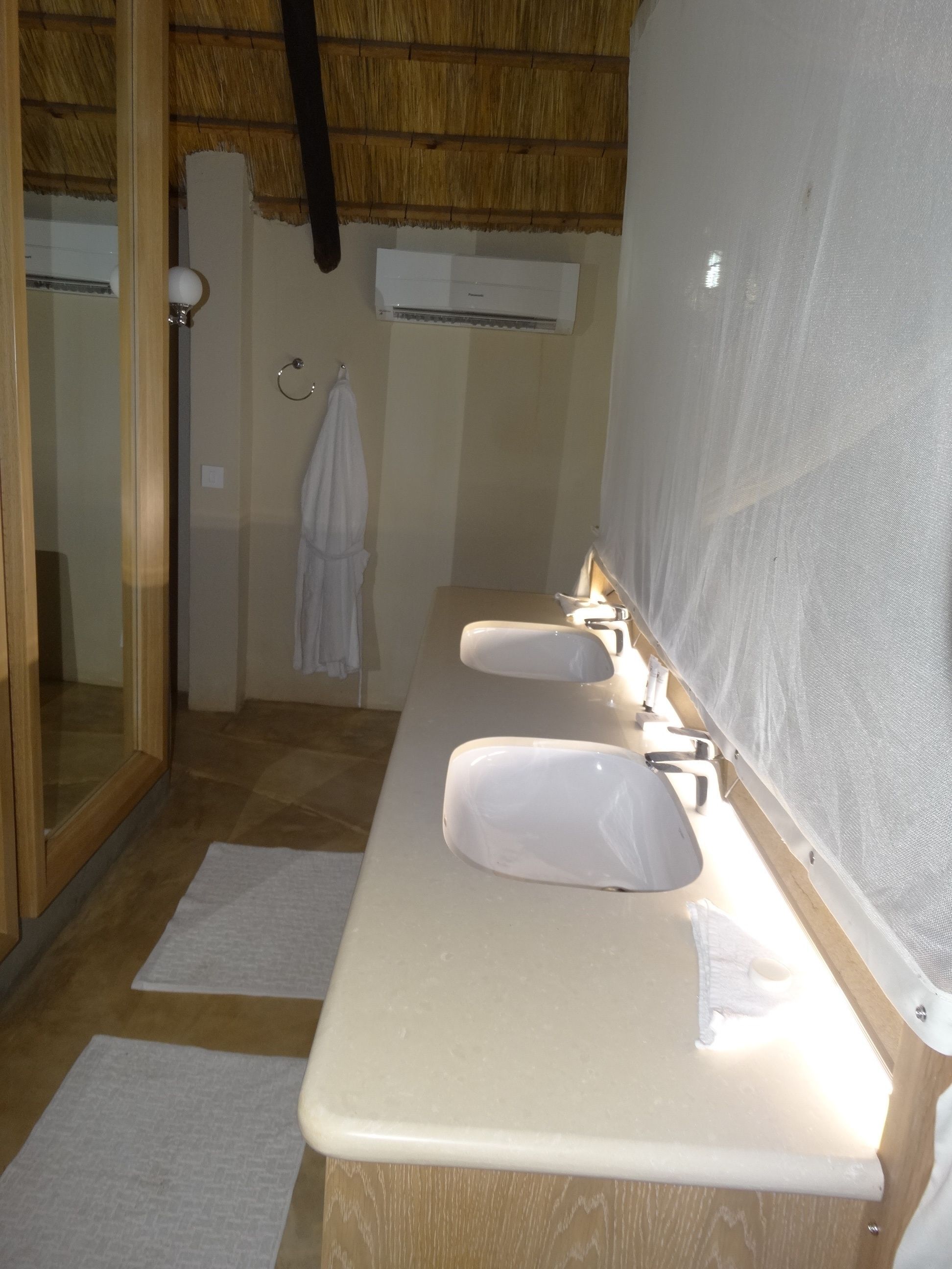 A bathroom with a wooden ceiling, a large mirror, two sinks, and a towel rack.
