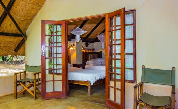 A rustic room with a bed, a wooden chair, and a thatched roof. - The Royal Sichango Village (Livingstone)