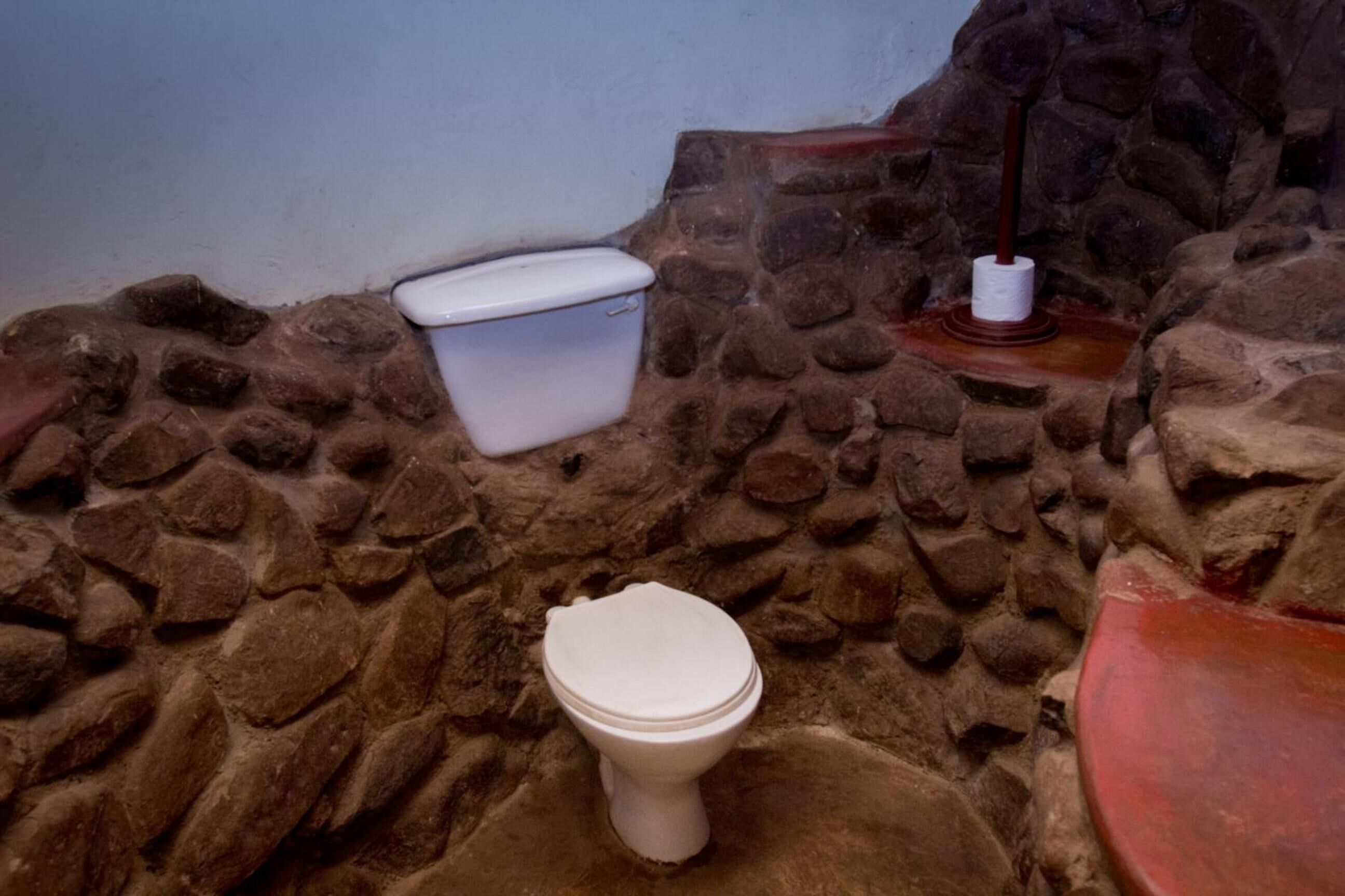 Un baño con pared de piedra, inodoro blanco y lavabo rojo.