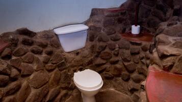 Un baño con pared de piedra, inodoro blanco y lavabo rojo.