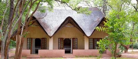 A traditional house with a thatched roof, surrounded by trees and a grassy area.
