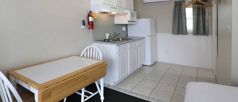 A compact kitchenette with a microwave, sink, and white cabinets. There is a small dining table with chairs and a bed in the room.