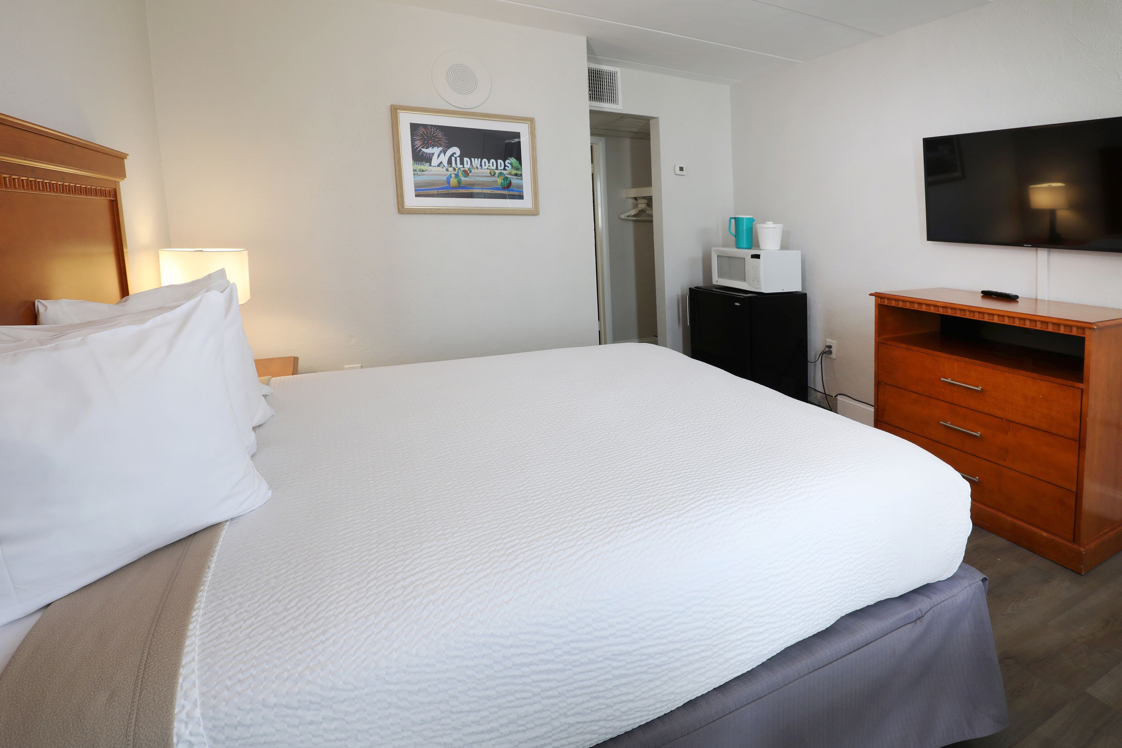 A hotel room with a large bed, a television, a small desk, and a framed picture on the wall.