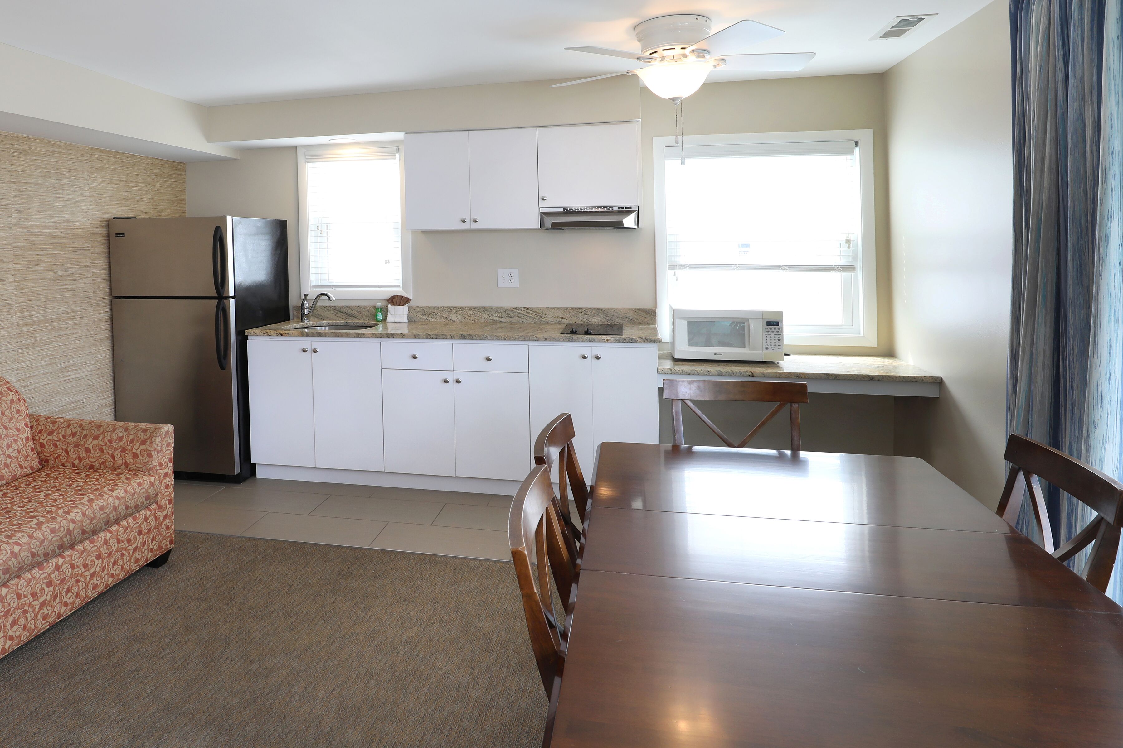 A modern kitchen with white cabinets, a stainless steel refrigerator, a microwave, and a dining area with a wooden table and chairs.