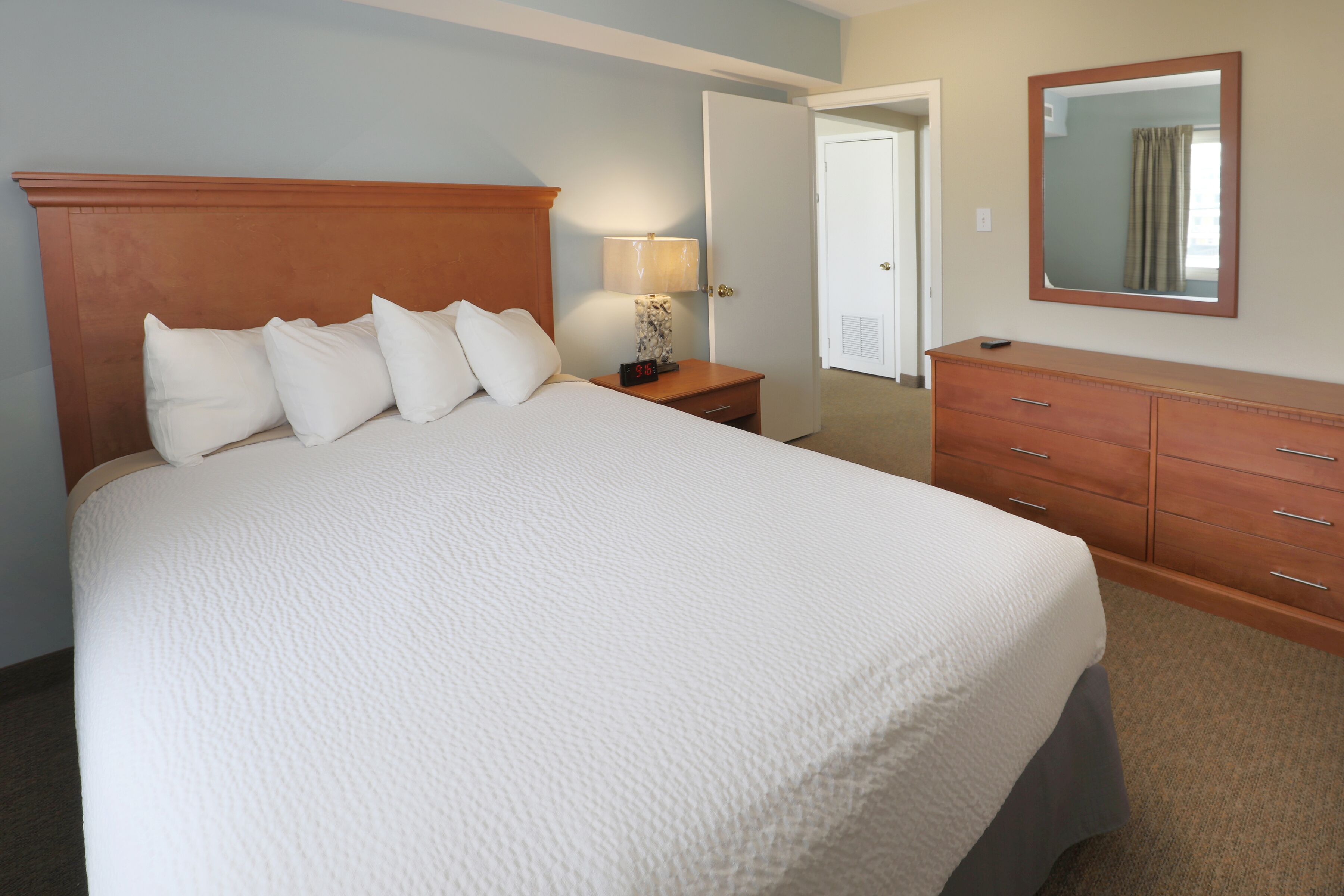 A hotel room with a large bed, a nightstand with a lamp, a dresser, and a mirror on the wall.