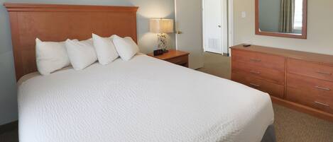 A hotel room with a large bed, a nightstand with a lamp, a dresser, and a mirror on the wall.