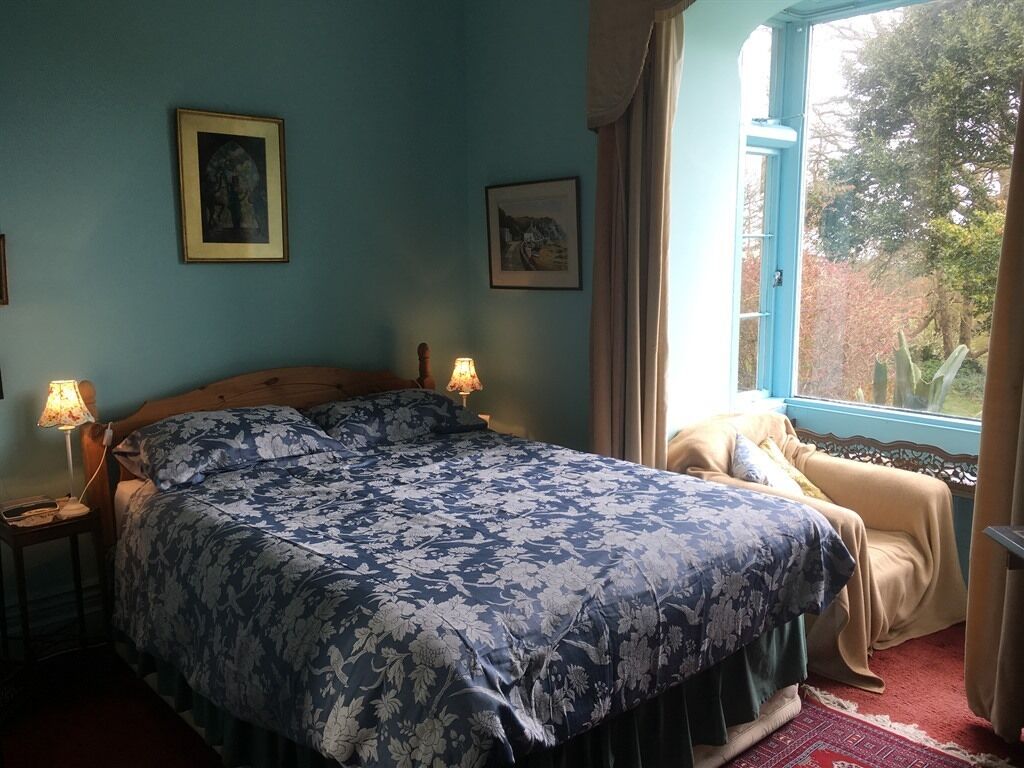 A bedroom with a large bed, two bedside lamps, a window with curtains, and two framed pictures on the wall.