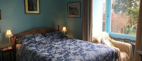 A bedroom with a large bed, two bedside lamps, a window with curtains, and two framed pictures on the wall.