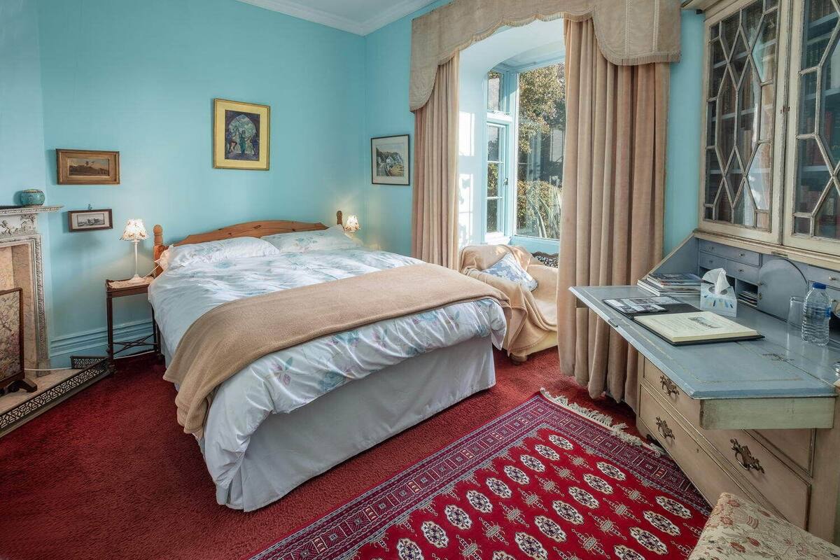 A bedroom with a large bed, a desk, and a window with curtains.