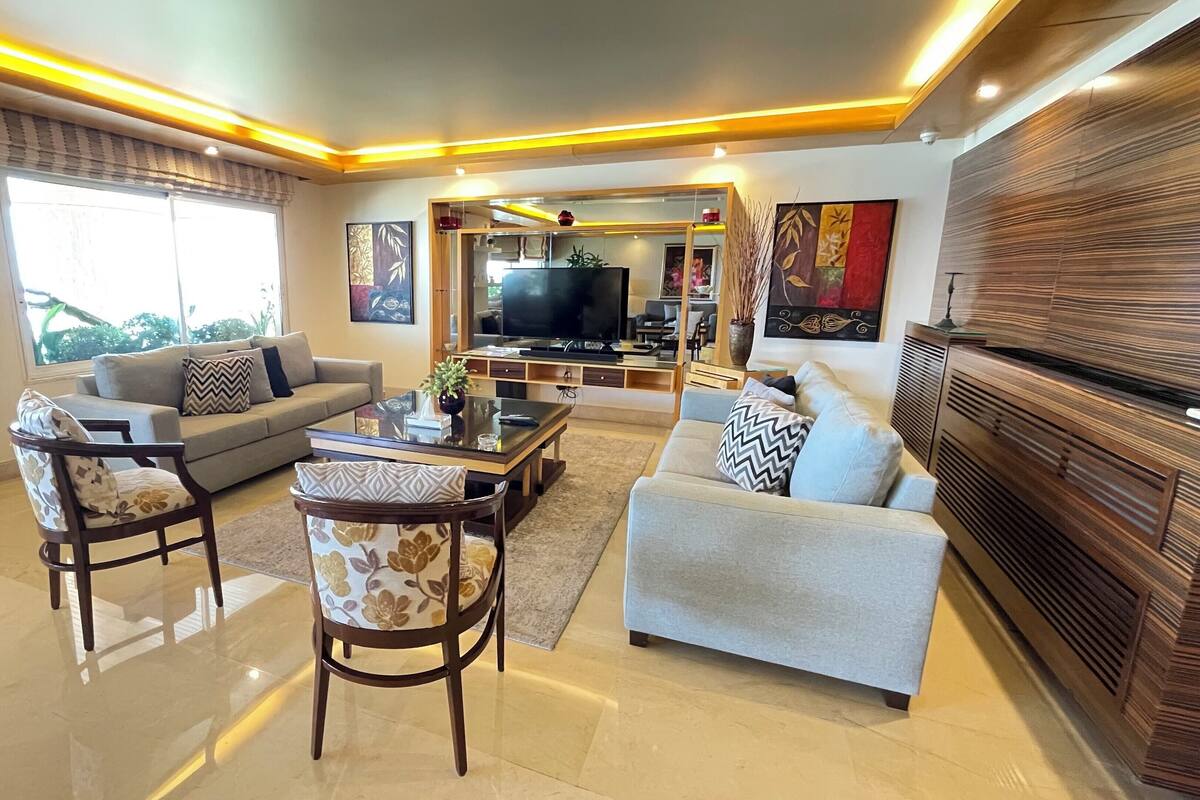A modern living room with a sofa, two armchairs, a coffee table, and a TV.