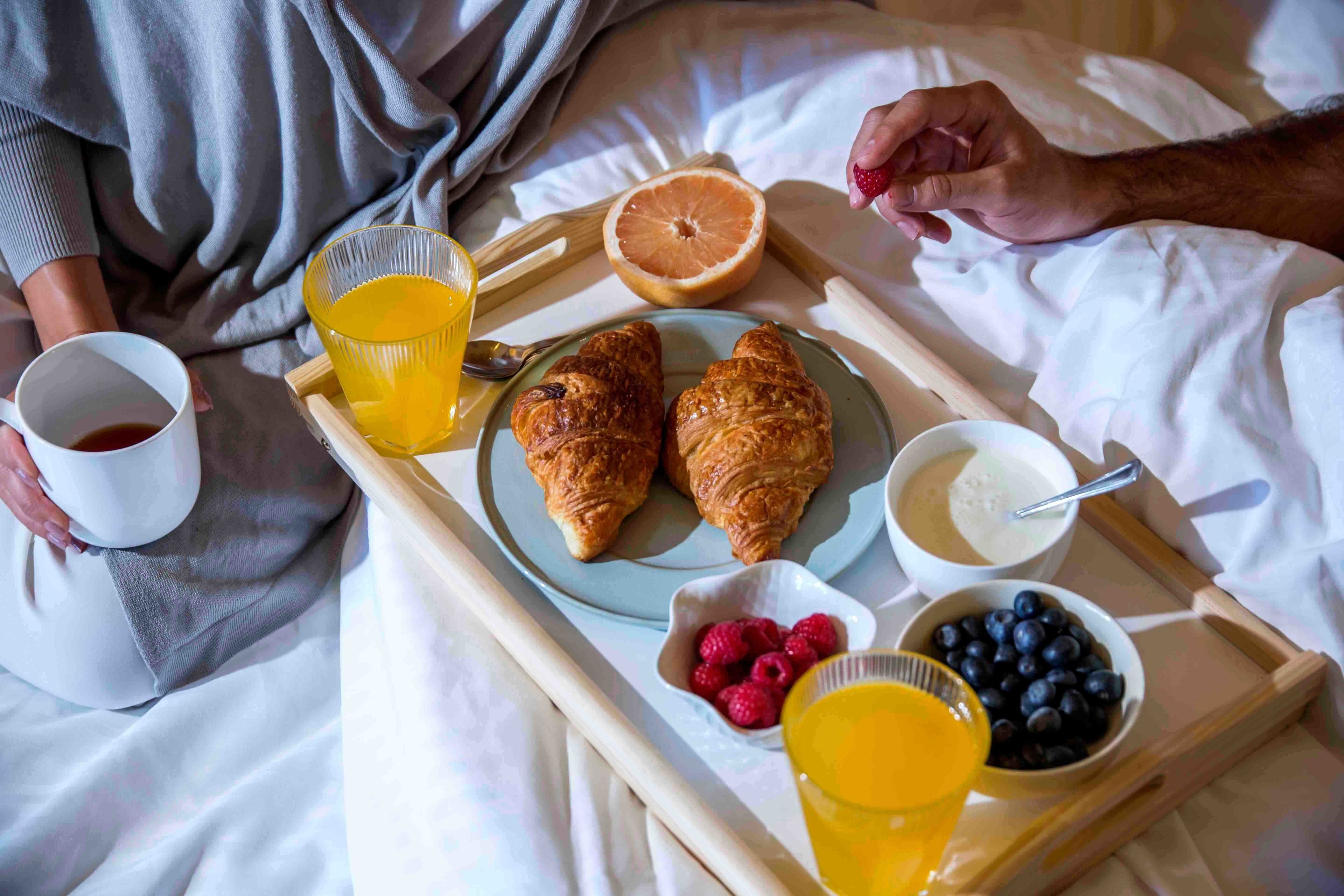 Un plateau avec des croissants, du jus d’orange et des fruits rouges, le tout disposé sur un lit.