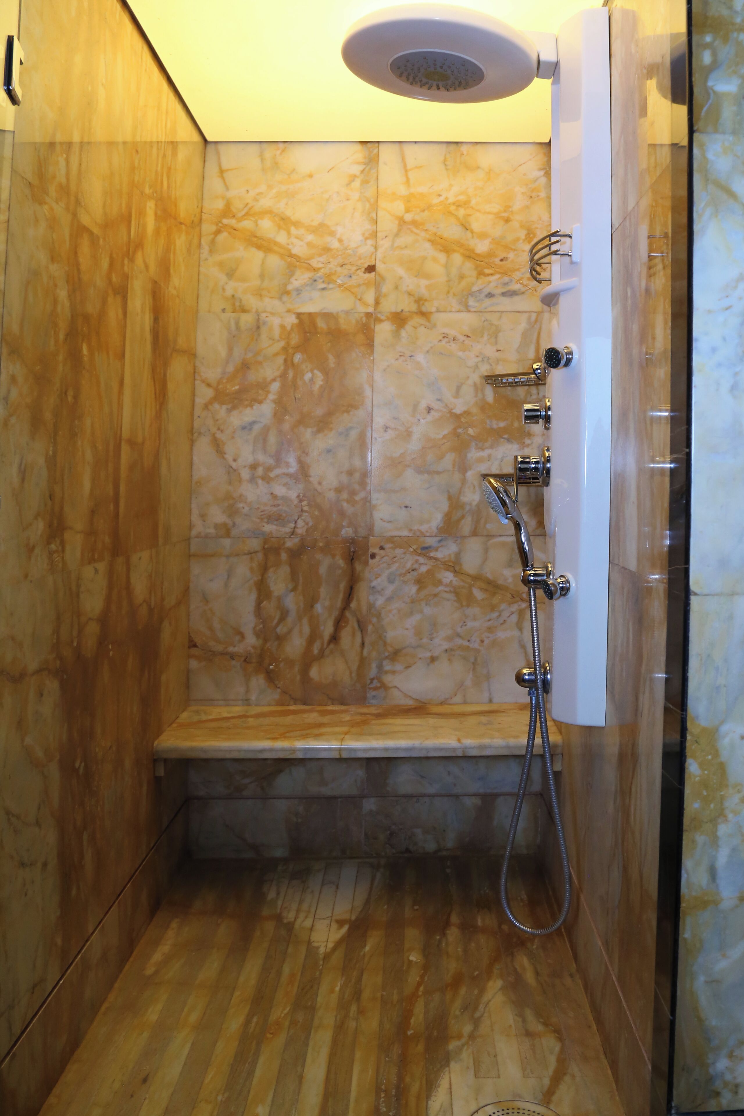 A shower with a bench, marble walls, and a wooden floor.