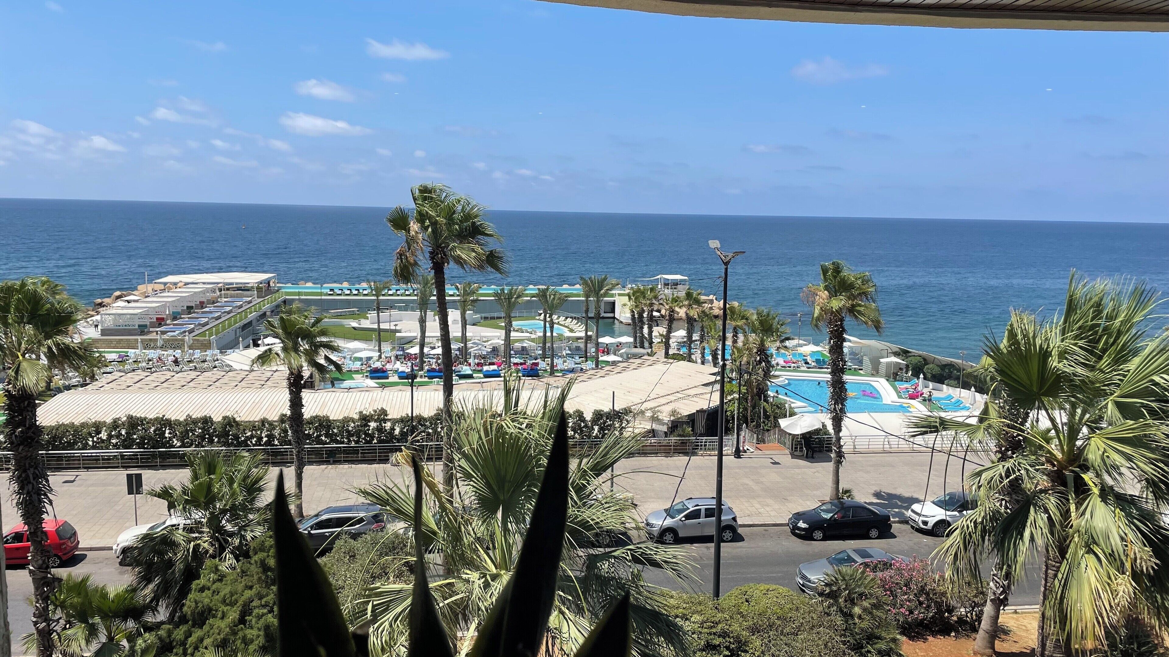 Un complejo turístico frente al mar con piscina, palmeras y vistas al océano.
