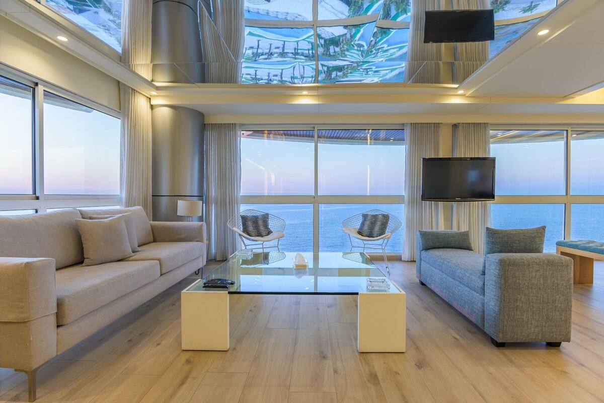 A modern living room with a glass coffee table, two sofas, and a TV mounted on the wall.