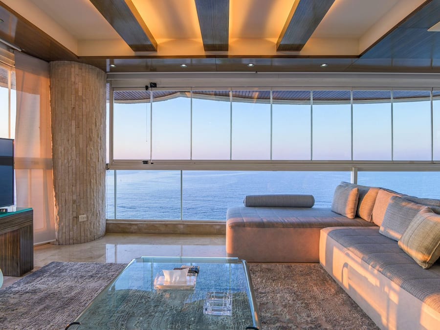 Una sala de estar moderna con un ventanal grande con vista al mar, un sofá, una mesa de centro y una televisión.