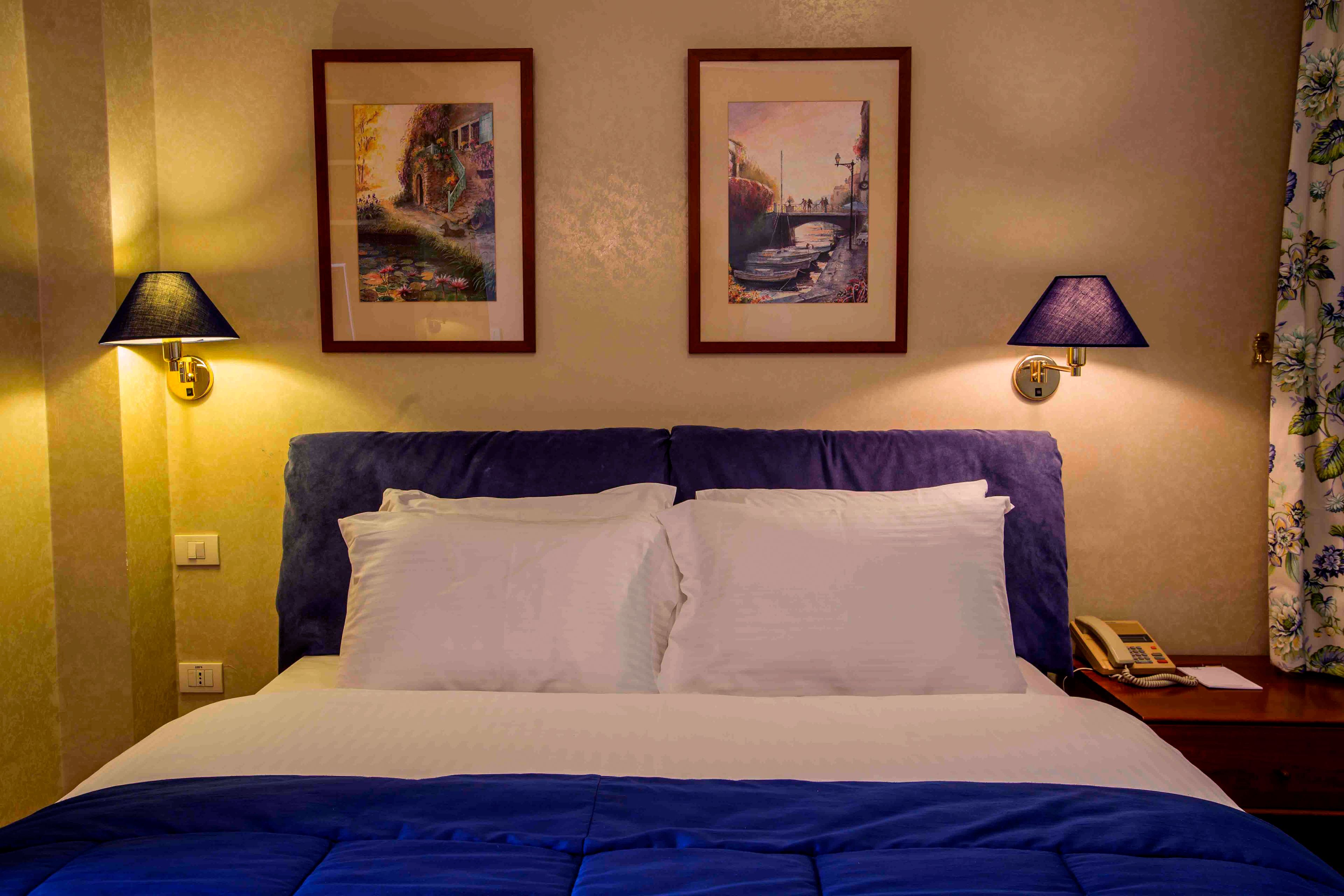 A hotel room with a bed, two wall-mounted lamps, and two framed pictures.