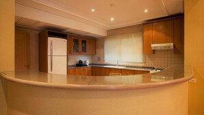 A kitchen with a curved countertop, wooden cabinets, a built-in refrigerator, and a window with blinds. - Lahoya Homes (Beirut)