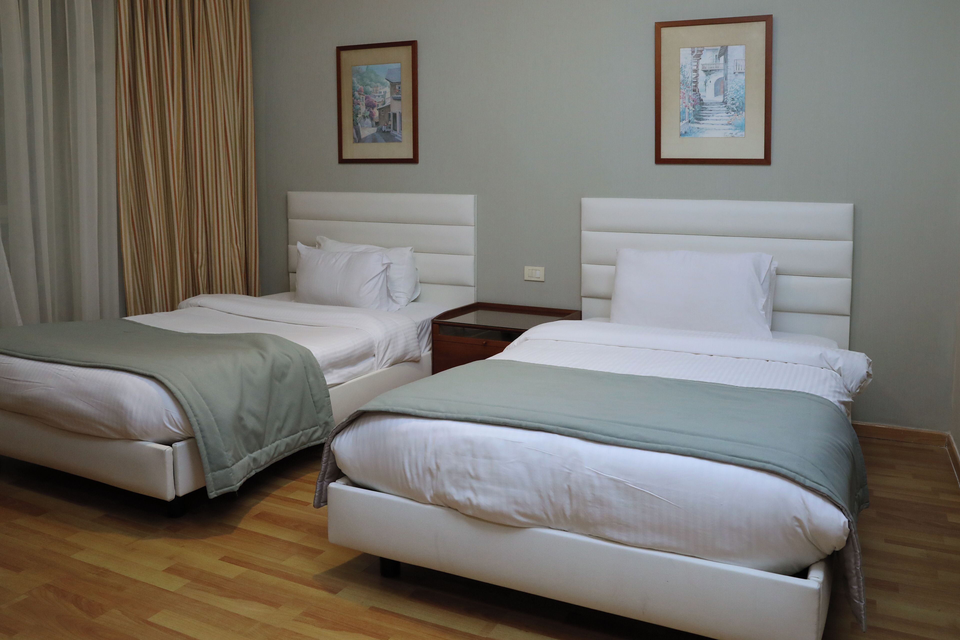 Habitación de hotel con dos camas, suelo de madera y dos cuadros en la pared.