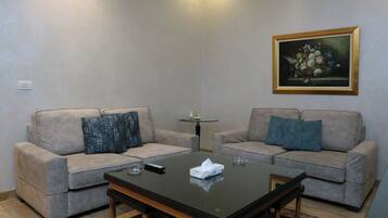A living room with two sofas, a coffee table, a painting on the wall, and a small table with a lamp.