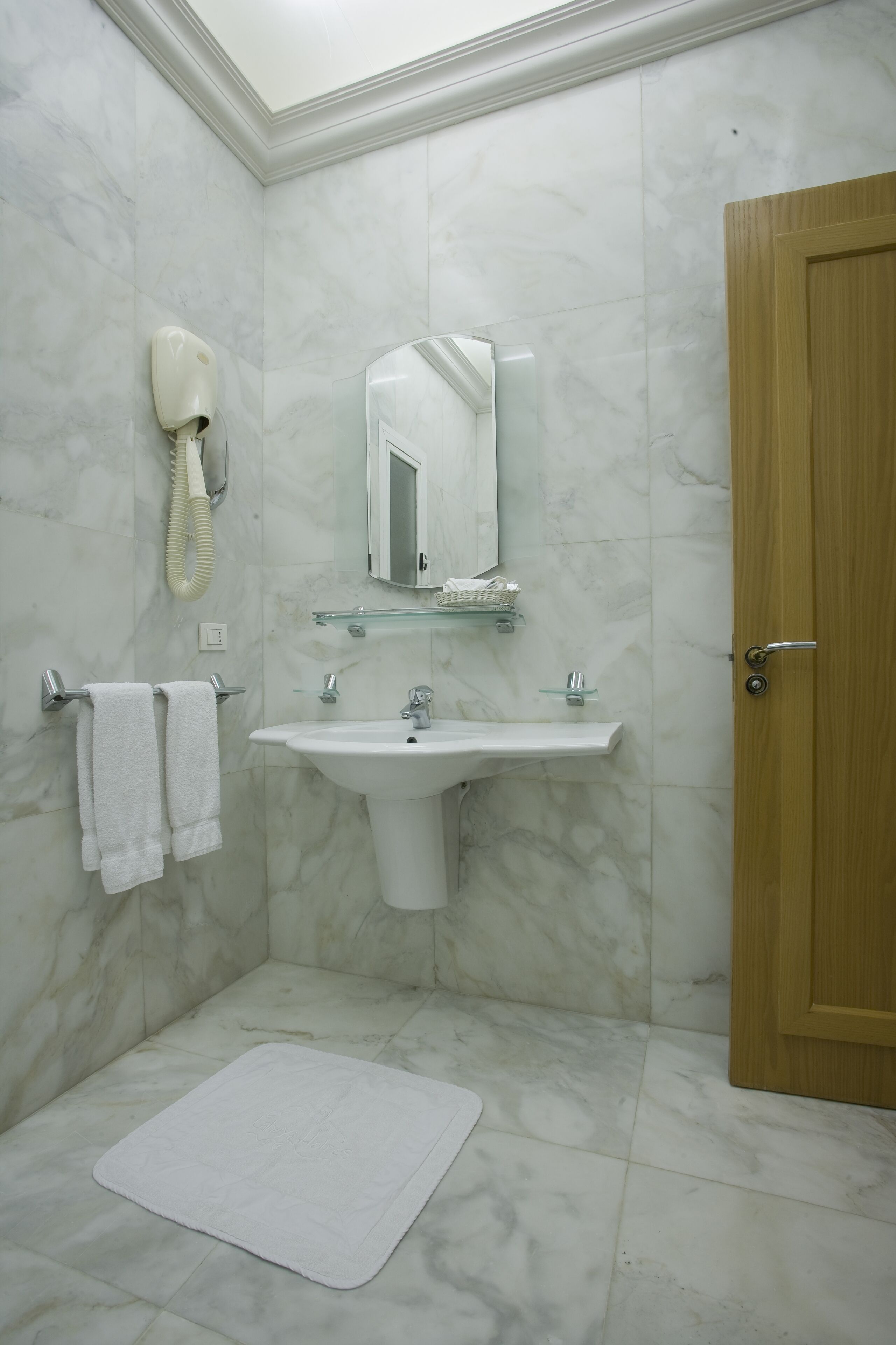 Un baño con suelo de mármol, un lavabo, un espejo, un perchero para toallas y una puerta de madera.