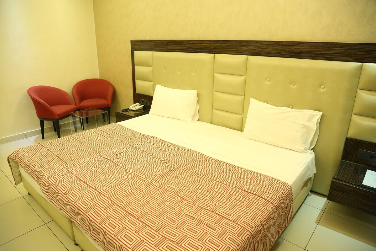 Una habitación de hotel con una cama grande, dos sillas rojas, una mesita y una mesilla de noche.