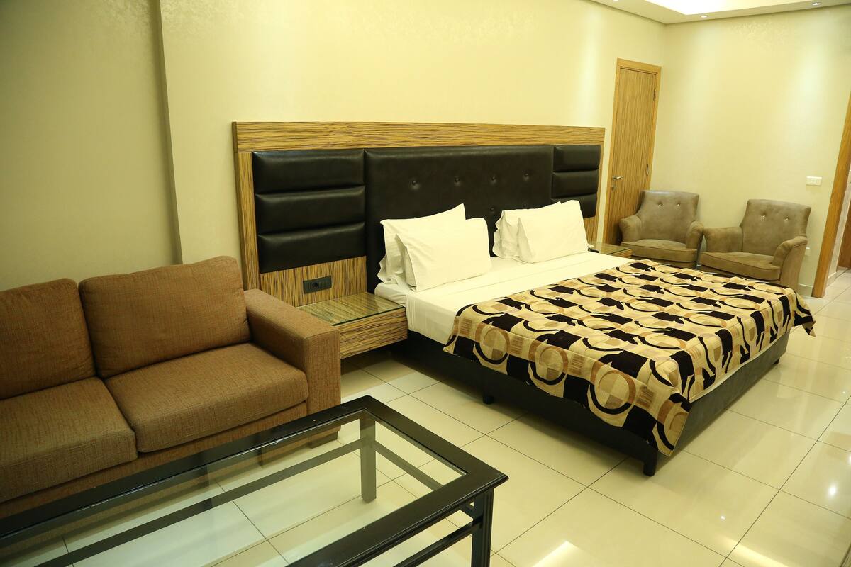 Una habitación de hotel con una cama, un sofá, una mesa de centro de vidrio y dos sillones.