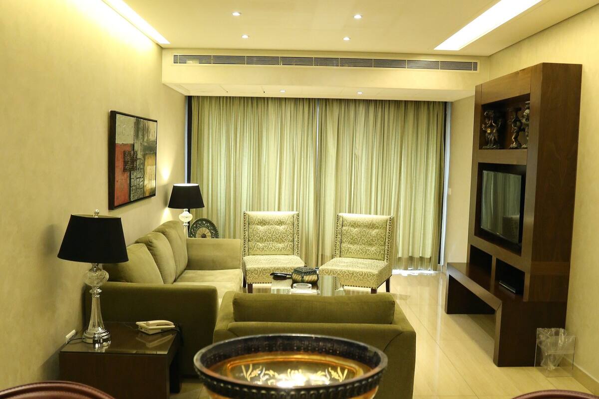 Una sala de estar moderna con un sofá, sillones, una mesa de centro y un televisor montado en la pared.