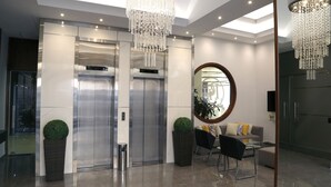 A modern lobby with two elevators, a round mirror, a sofa, and a chandelier. - Verdun Suites Hotel (Beirut)
