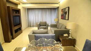 A hotel room with a TV, a sofa, a chair, a lamp, and a decorative glass table centerpiece. - Verdun Suites Hotel (Beirut)