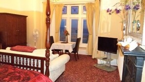 Une chambre d’hôtel avec un lit, un bureau équipé d’un ordinateur, une chaise, une table et une fenêtre avec des rideaux.