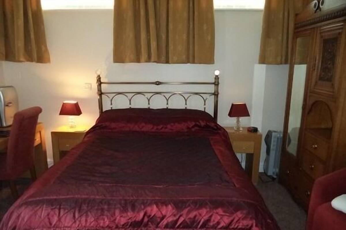 A room with a bed, two bedside tables with lamps, a chair, a wardrobe, and a window with curtains.