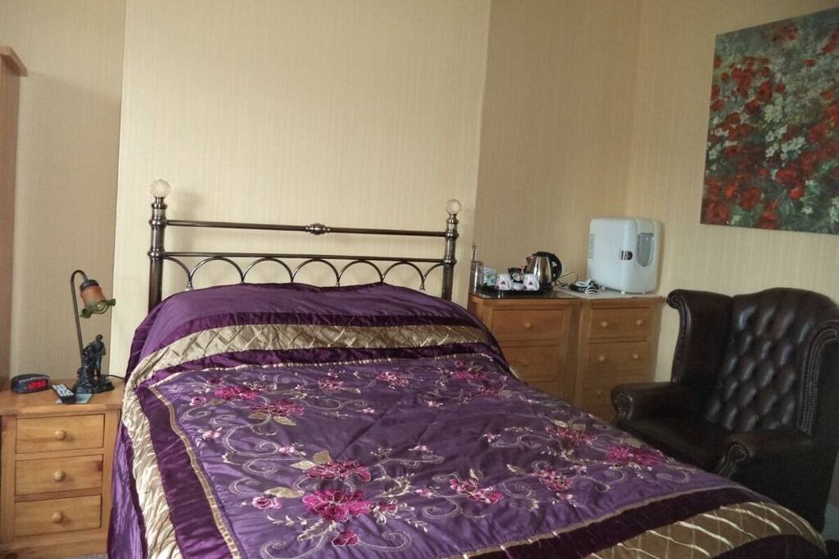 A bedroom with a bed, a nightstand, a desk, a chair, and a painting on the wall.