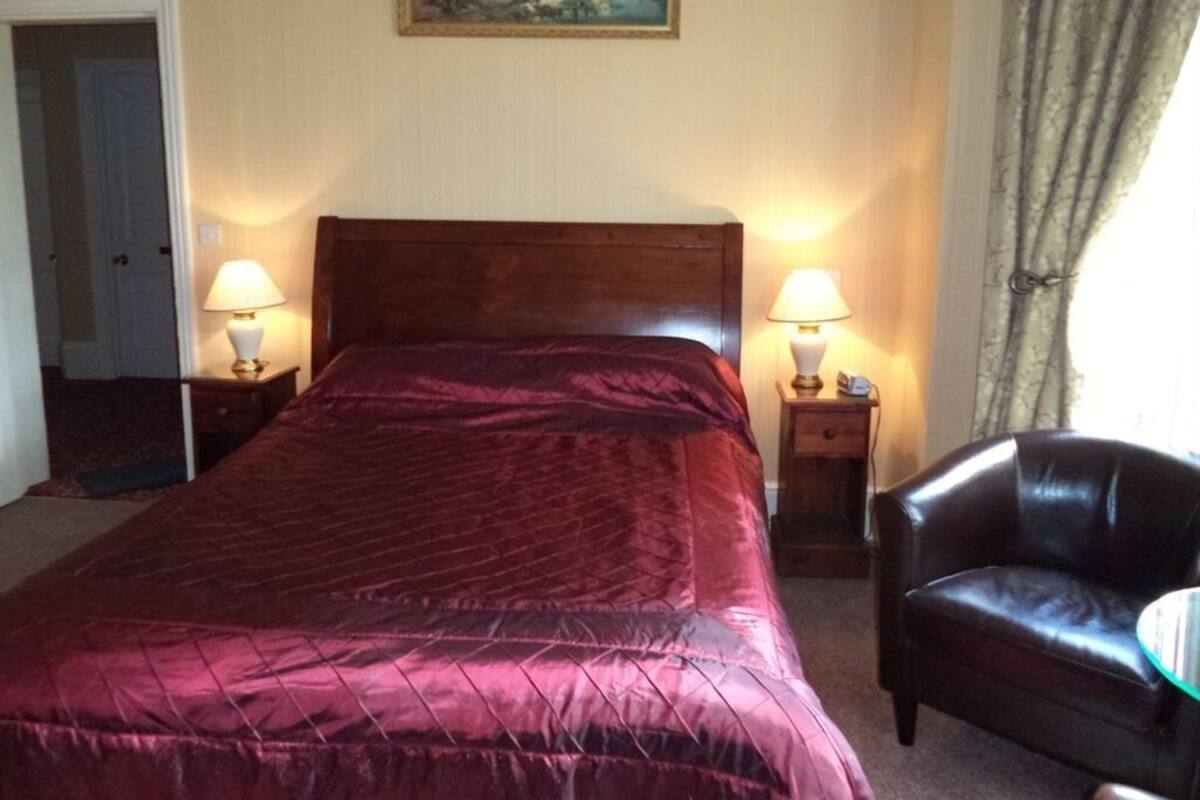 A hotel room with a large bed, two bedside lamps, a chair, a painting on the wall, and a door.