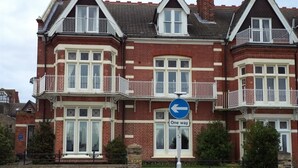 Une maison à deux étages, aux murs en briques rouges, dotée de fenêtres à cadre blanc et d’un balcon.