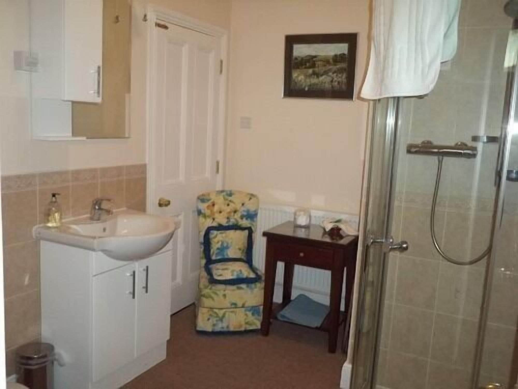 A bathroom with a sink, mirror, shower, and a chair with a towel.