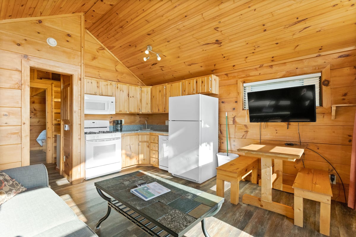 A wooden cabin with a kitchen, dining area, and a living room with a sofa.