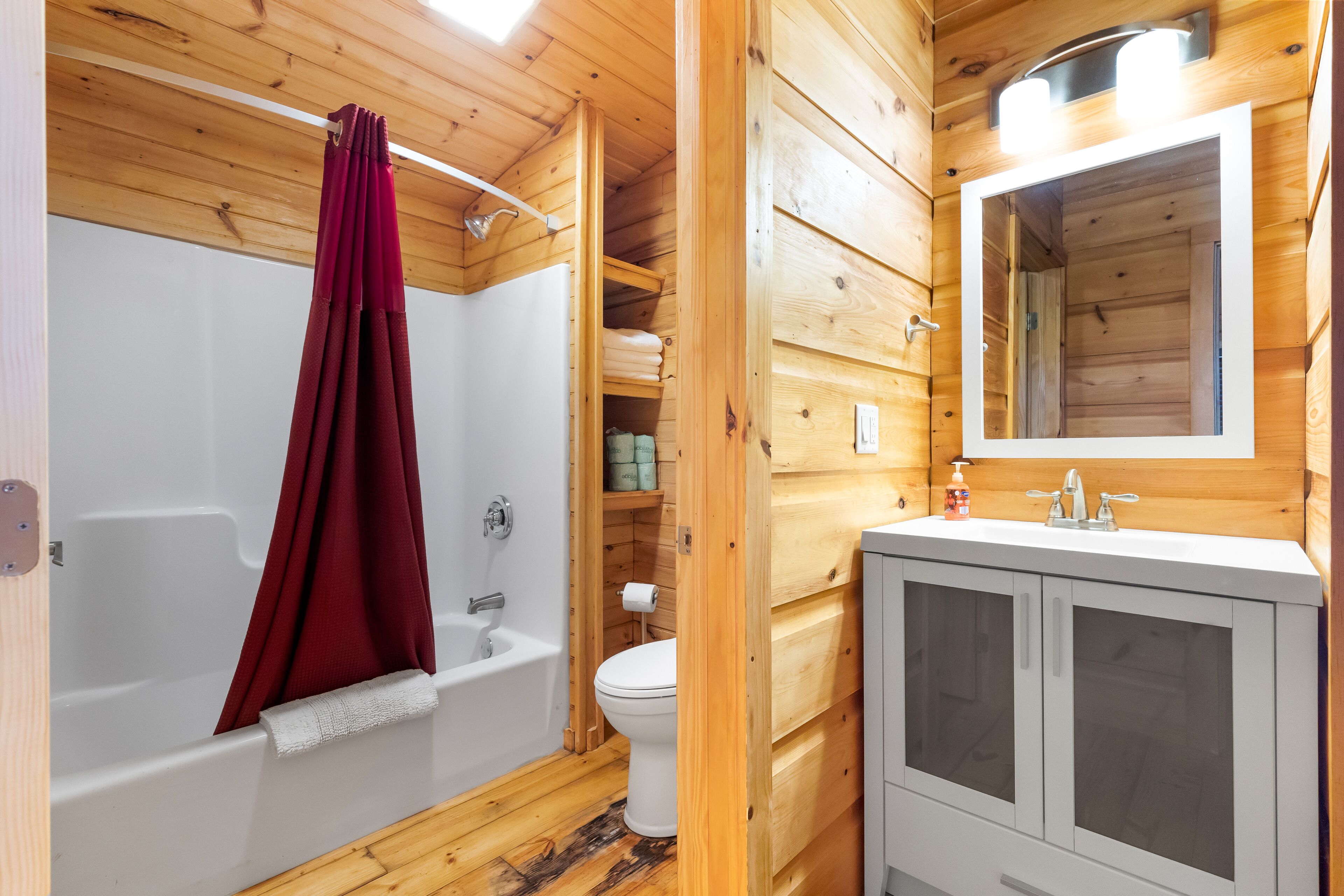 A wooden cabin bathroom with a bathtub, toilet, and a vanity with a mirror.