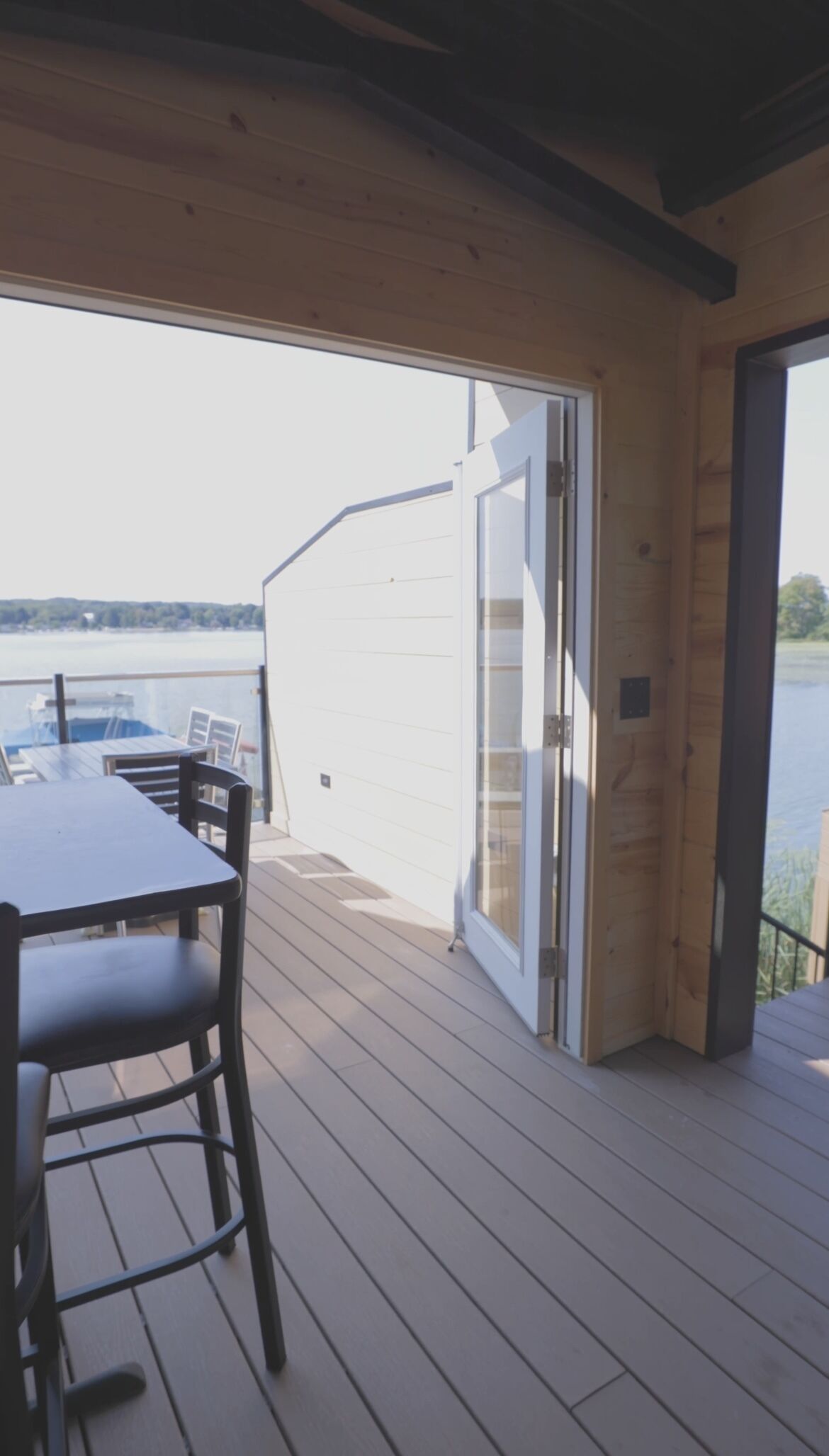 A wooden deck with a table and chairs, a sliding glass door leading to a view of a body of water, and a boat docked nearby.