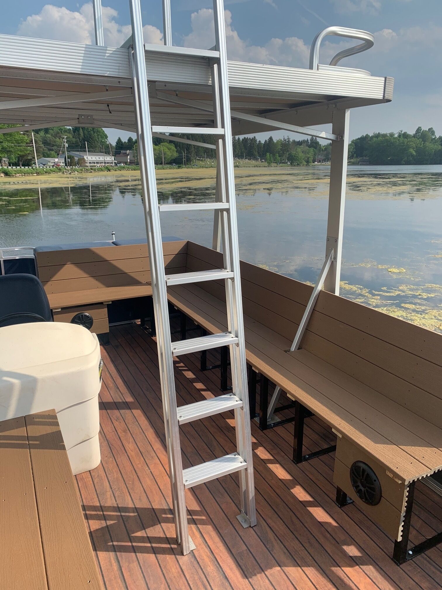 A boat deck with a metal ladder, wooden benches, and a white container.