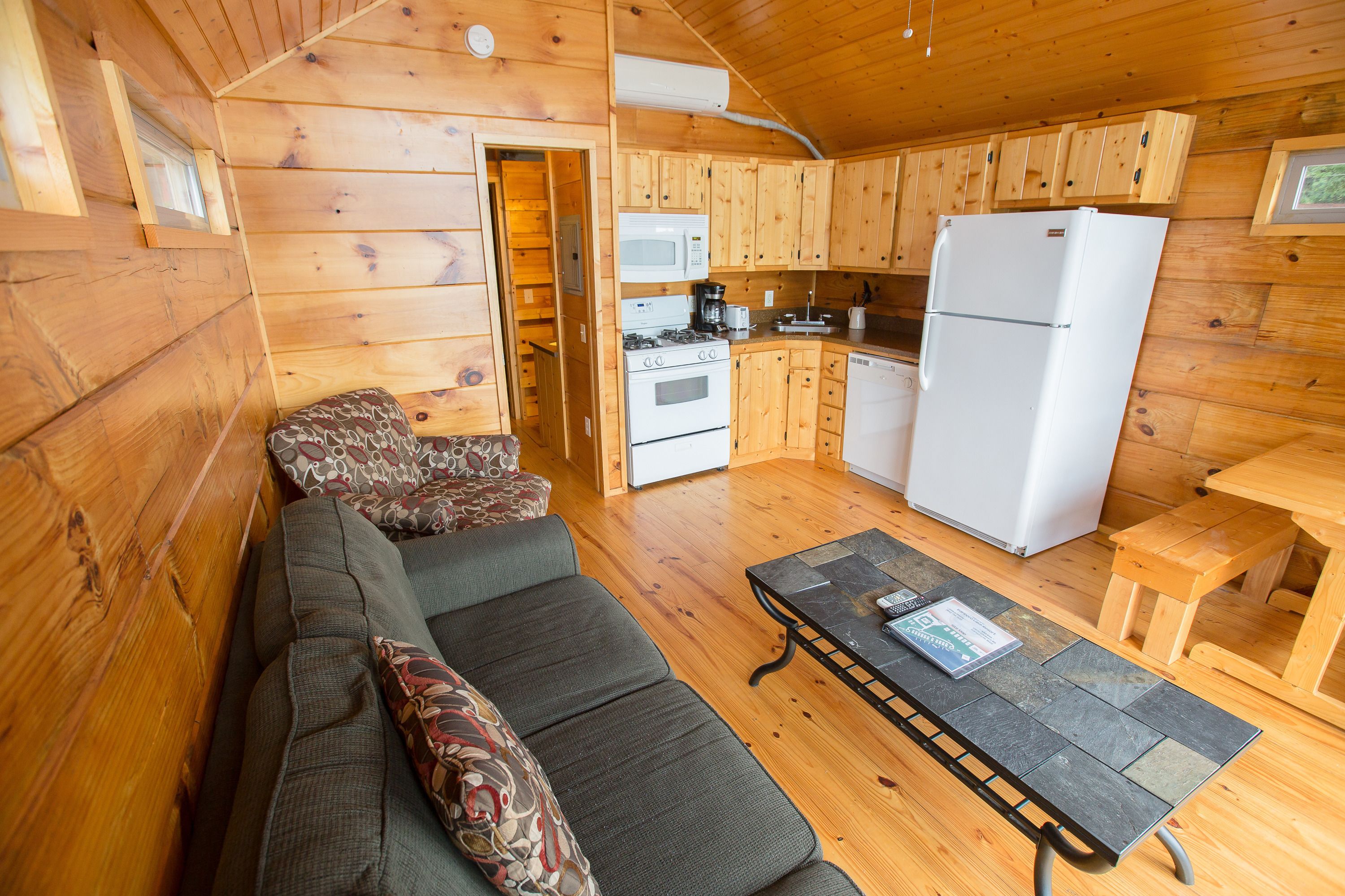 A cozy cabin-style room with a sofa, a dining table, a kitchen area with a stove, microwave, and refrigerator.