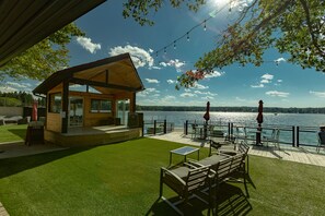 A wooden cabin with a deck overlooking a lake, furnished with outdoor seating and a table.