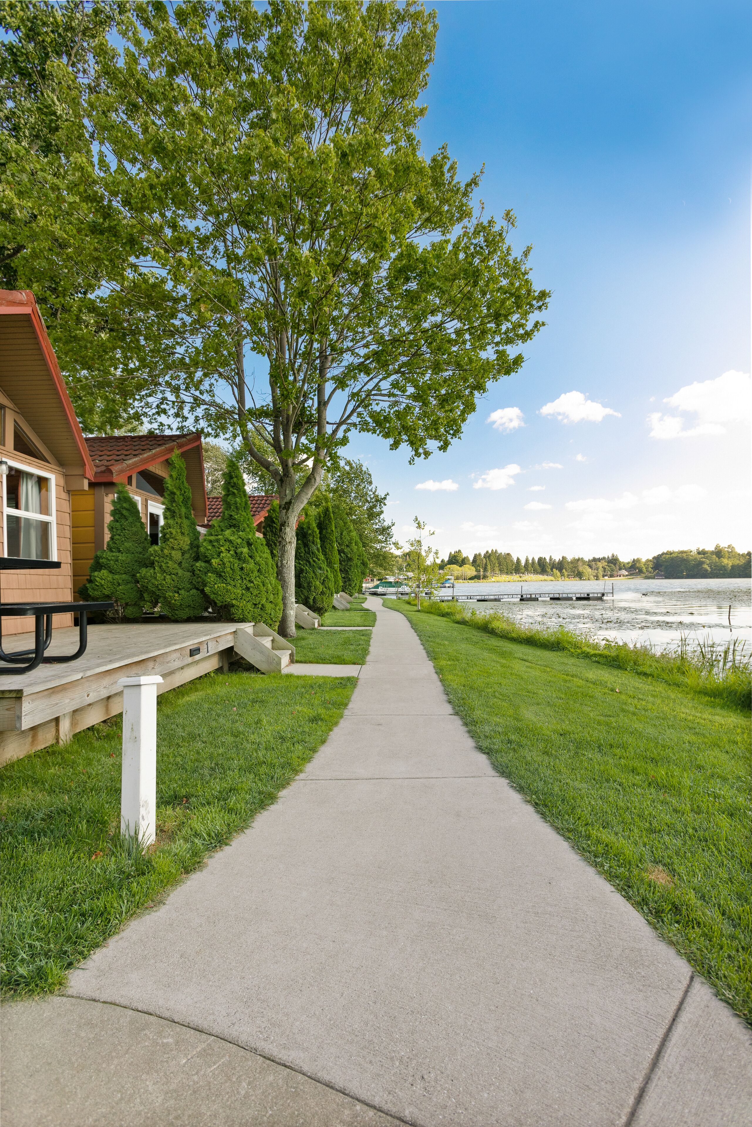 A pathway leading to a lakeside cabin with a picnic table and a dock.