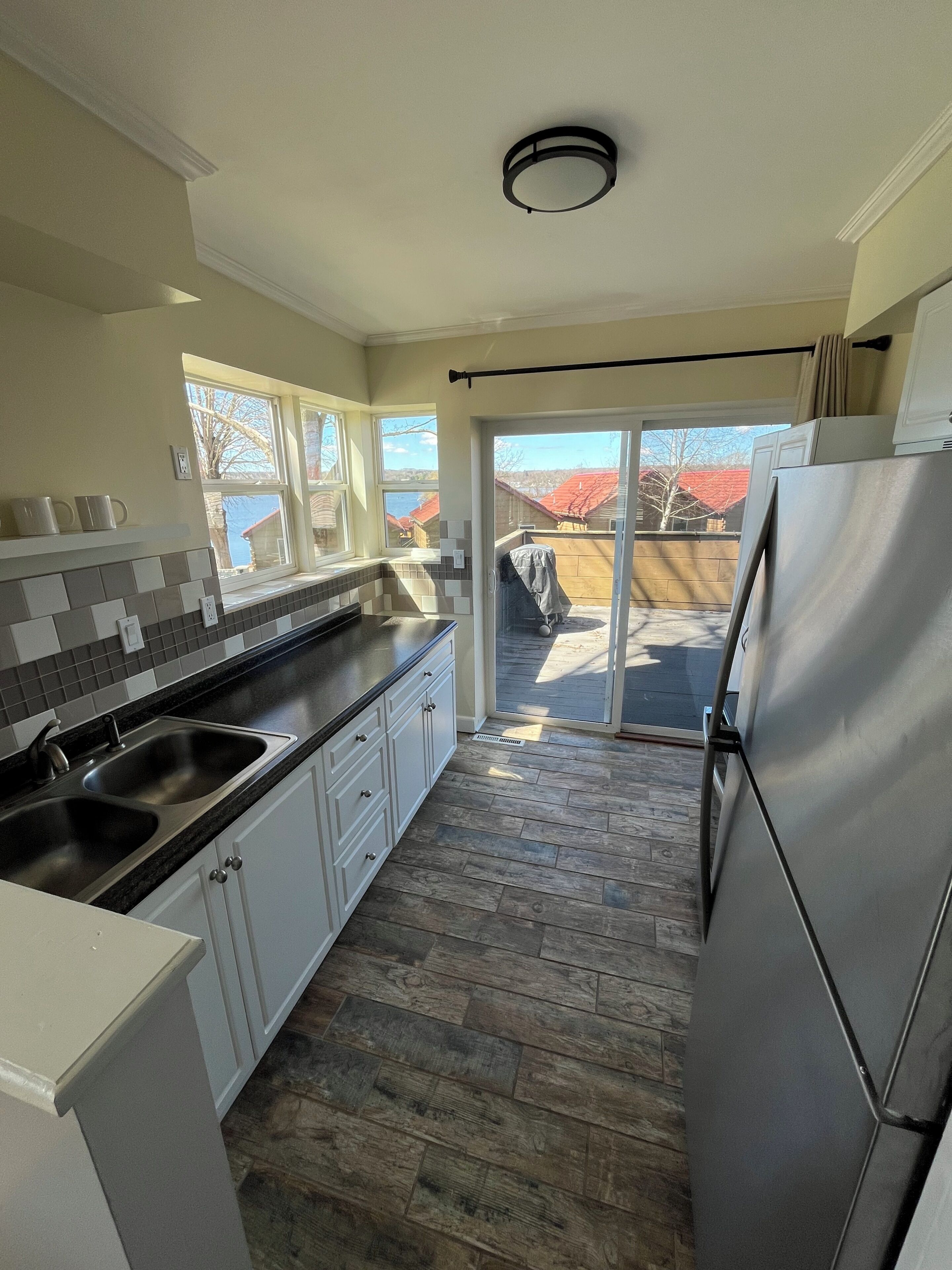 A kitchen with a double sink, white cabinets, a stainless steel refrigerator, and a view of a red-roofed building outside.
