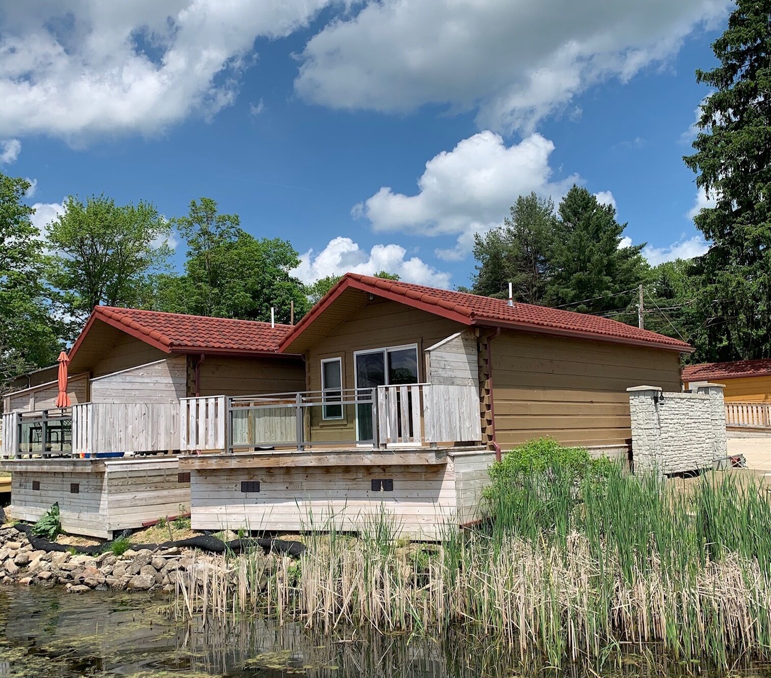 Une cabane en bois avec un toit rouge, une terrasse et un mur en pierre.