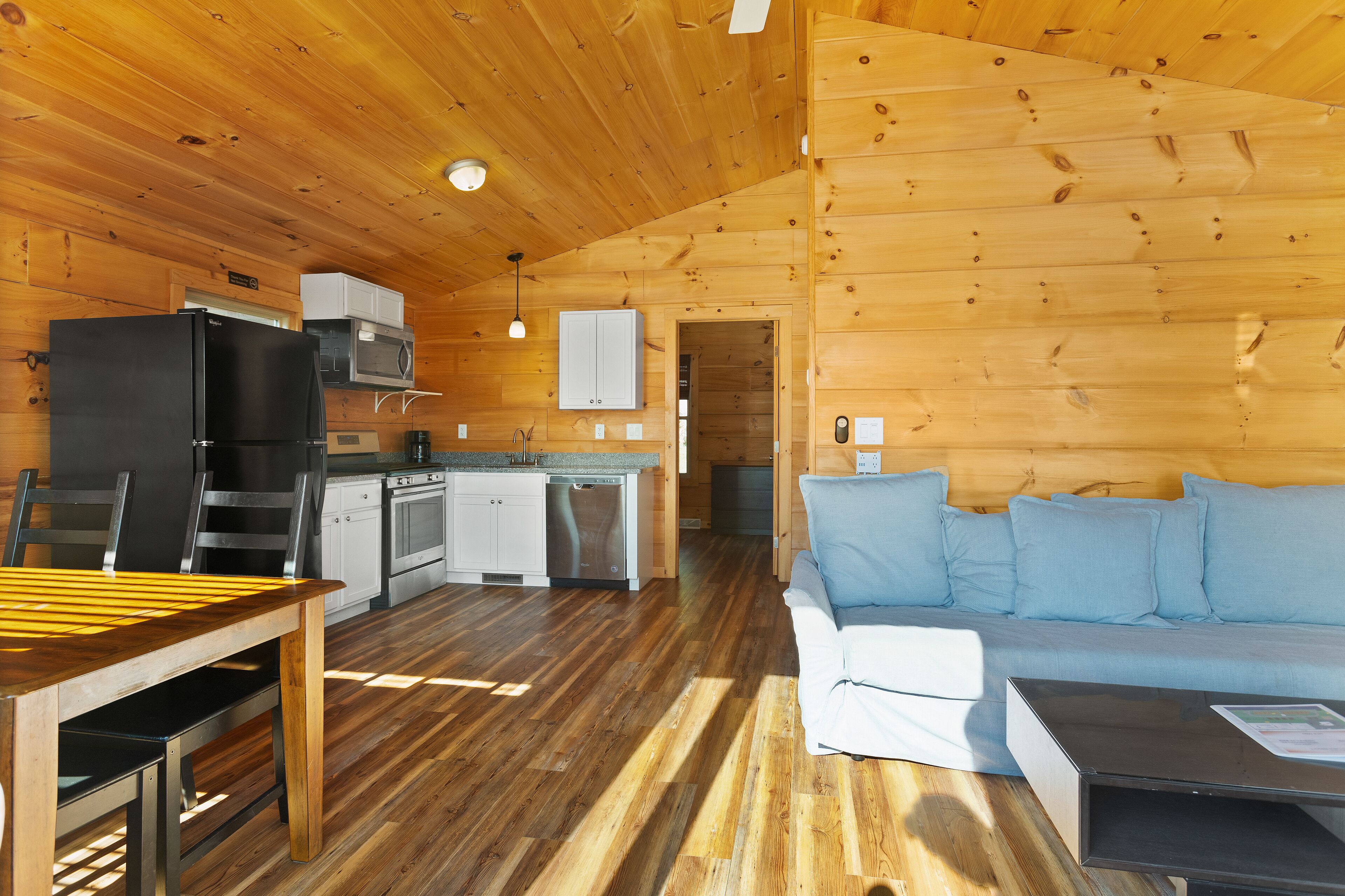 Interior d'una cabana de fusta amb taula de dinar, zona de cuina i un sofà.