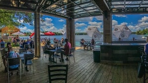 An outdoor dining area with tables and chairs, umbrellas, and a view of a lake. - Edinboro Lake Resort Cabins (Edinboro)
