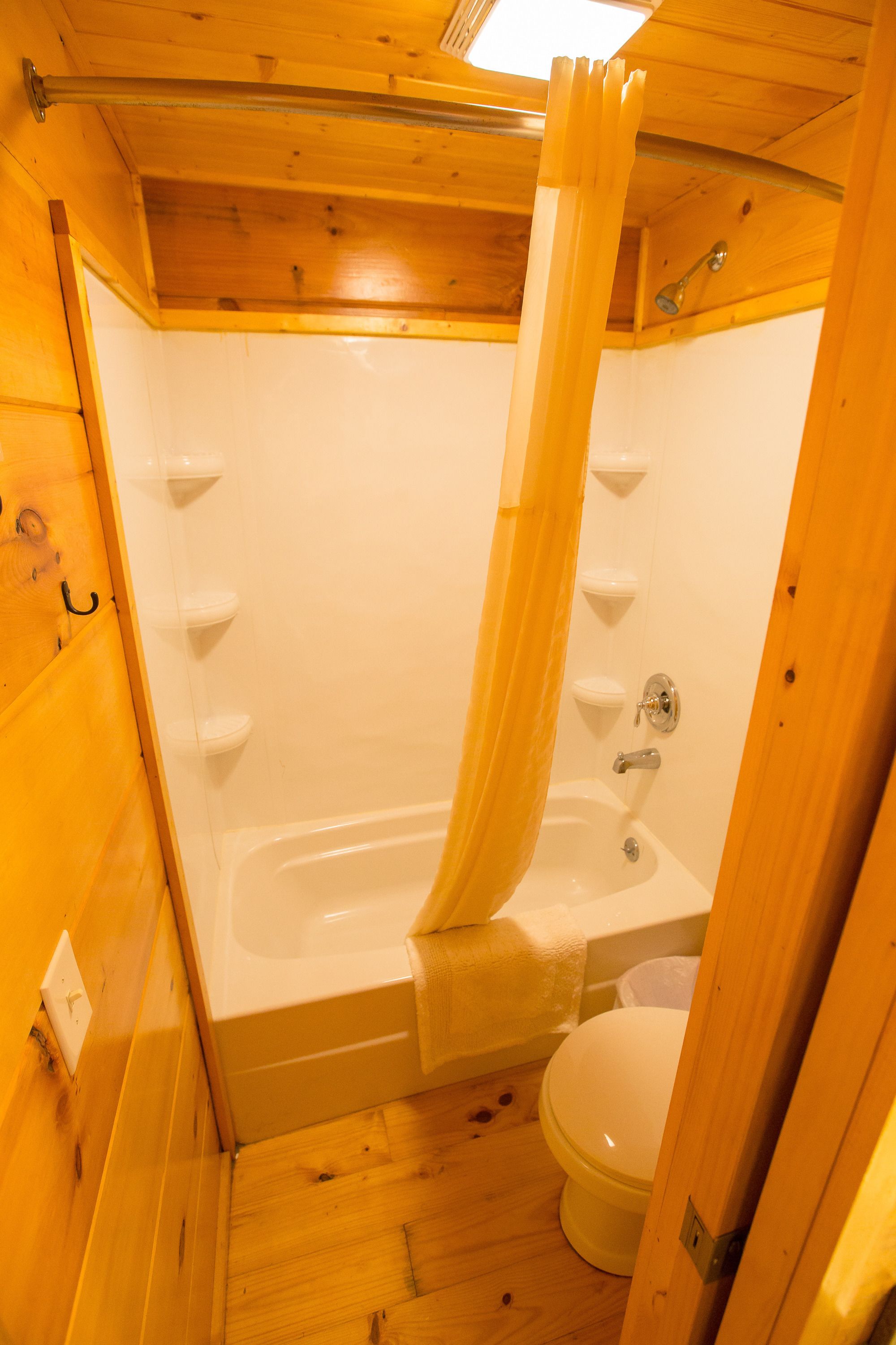 A small, wooden bathroom with a bathtub, toilet, and a shower curtain.