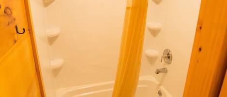 A small, wooden bathroom with a bathtub, toilet, and a shower curtain.