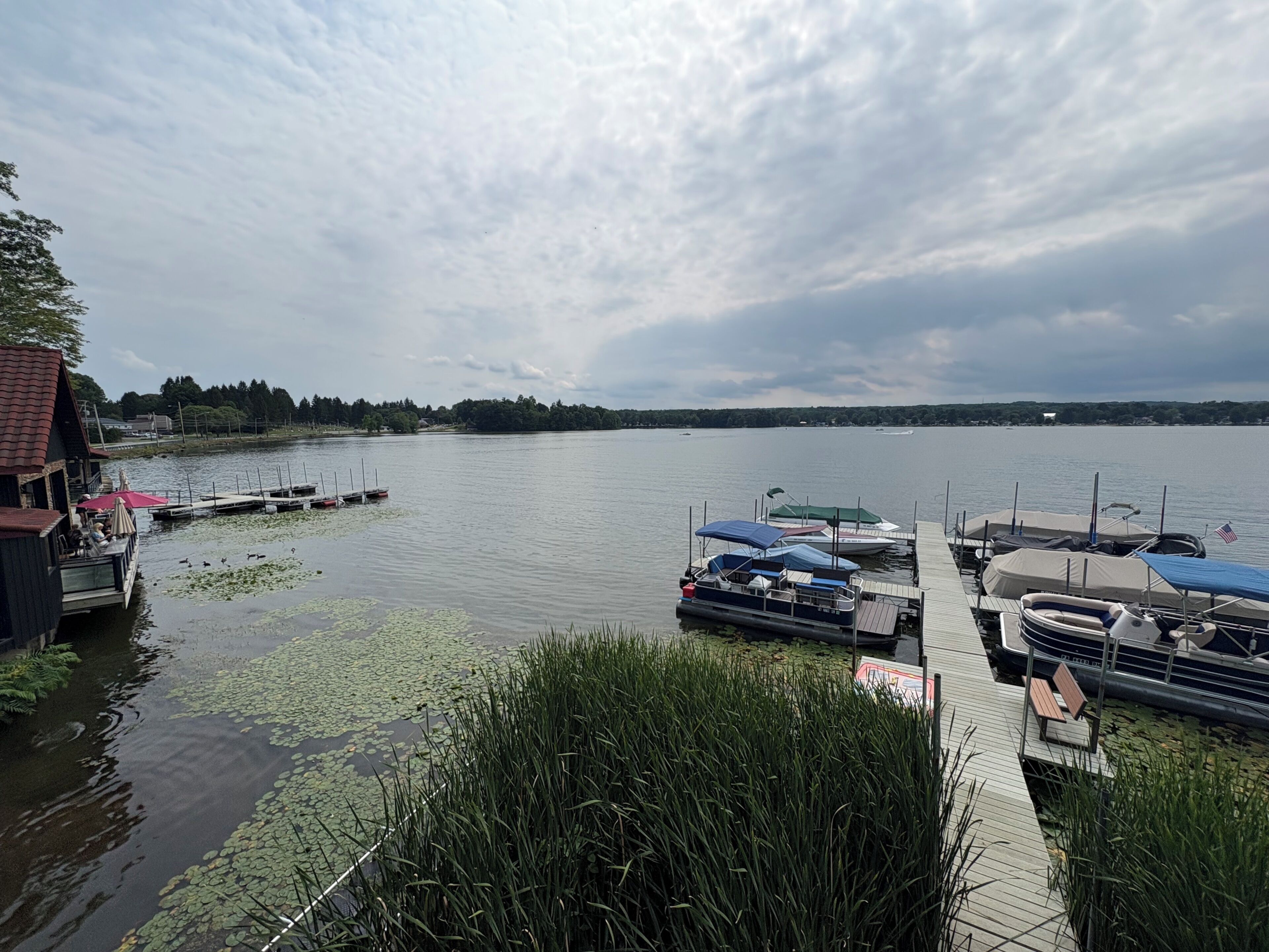 Une jetée au bord du lac avec des bateaux, une plateforme en bois et un bâtiment doté d’une terrasse.